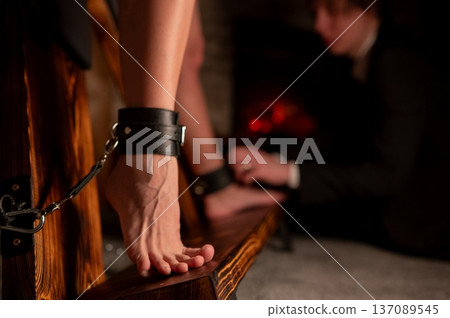 A man chains a woman's legs to a BDSM cross. 137089545