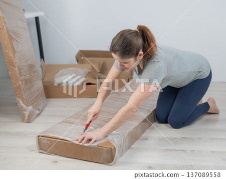 A Caucasian woman unpacks a box of furniture. A Caucasian woman unpacks a box of furniture. 137089558