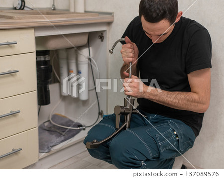 A plumber is replacing a faucet in the kitchen. A plumber is replacing a faucet in the kitchen. 137089576
