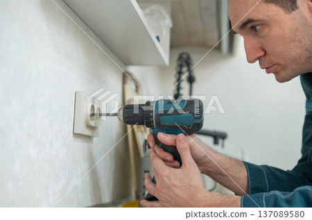 An electrician unscrews a socket with a screwdriver. An electrician unscrews a socket with a screwdriver. 137089580