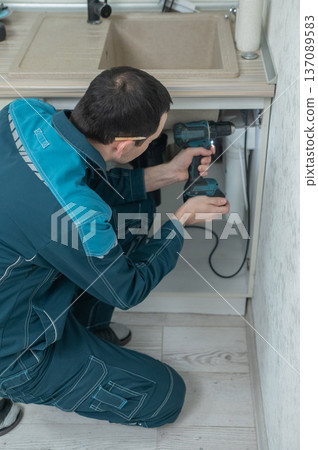 The technician removes the door from the kitchen cabinet. The technician removes the door from the kitchen cabinet. 137089583