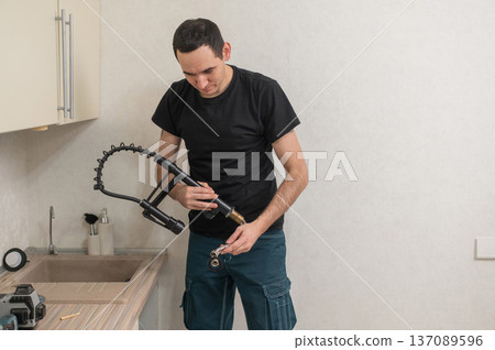 A plumber is replacing a faucet in the kitchen. 137089596
