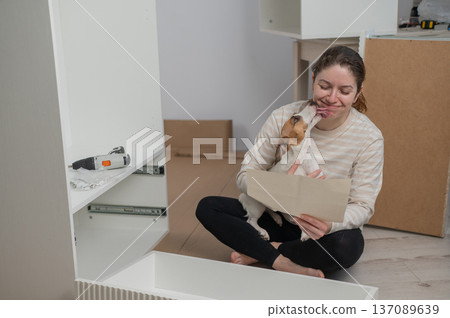 A Caucasian woman assembles furniture with her cute dog. A Caucasian woman assembles furniture with her cute dog. 137089639