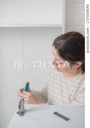 A Caucasian woman assembles a wardrobe. She understands the hardware. A Caucasian woman assembles a wardrobe. She understands the hardware. 137089640