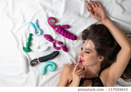 A beautiful Caucasian woman in black lingerie lies among sex toys.  137089643