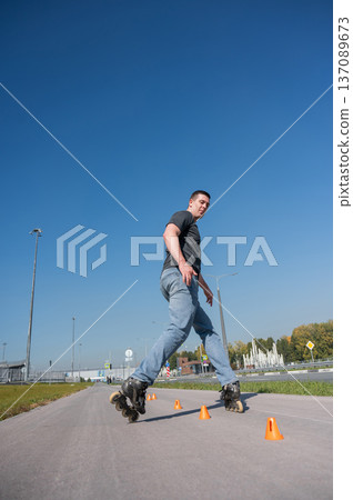 A Caucasian man rollerblades around the slalom course. A Caucasian man rollerblades around the slalom course. 137089673