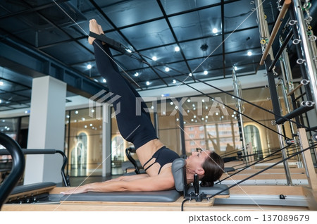 Caucasian woman doing exercises on reformer machine. Caucasian woman doing exercises on reformer machine. 137089679