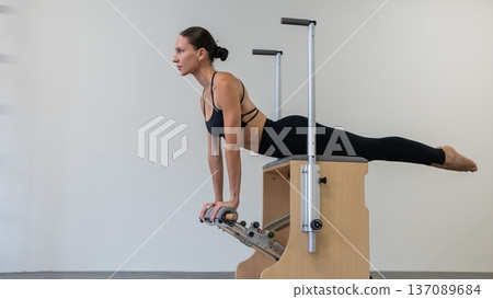 Caucasian woman doing Pilates on classic chair. Caucasian woman doing Pilates on classic chair. 137089684