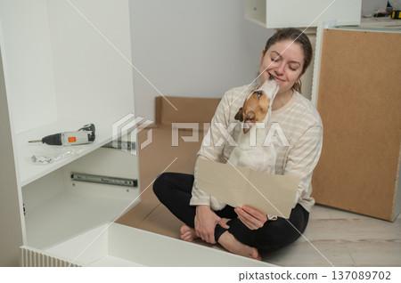 A Caucasian woman assembles furniture with her cute dog. A Caucasian woman assembles furniture with her cute dog. 137089702