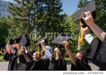 Young women of different nationalities pull graduation caps up. Young women of different nationalities pull graduation caps up. 137089742
