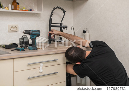 A plumber is replacing a faucet in the kitchen. A plumber is replacing a faucet in the kitchen. 137089781