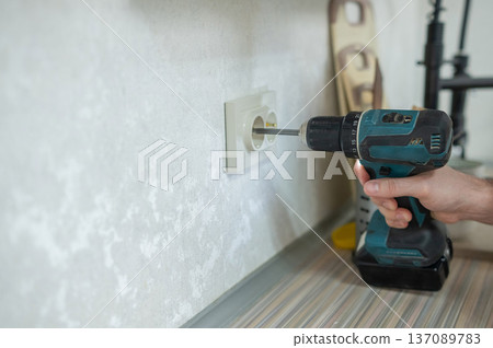 An electrician unscrews a socket with a screwdriver. An electrician unscrews a socket with a screwdriver. 137089783