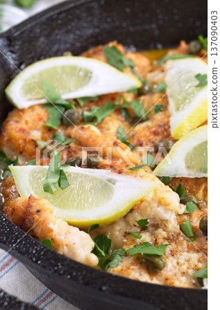 Haddock fish piccata with lemon and capers in cast iron pan, vertical closeup Haddock fish piccata with lemon and capers in cast iron pan, vertical closeup 137090403