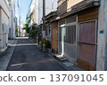 A narrow, sunlit, straight alley lined with old buildings and apartments 137091045
