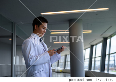 A man in a white coat operates a tablet A man in a white coat operates a tablet 137091759