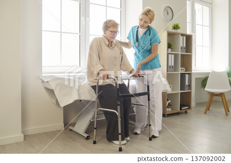 Nurse helping elderly woman stand from exam bed with walker in clinic for checkup Nurse helping elderly woman stand from exam bed with walker in clinic for checkup 137092002