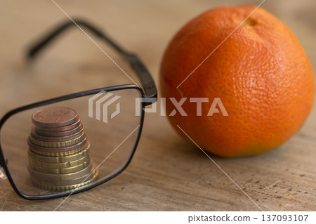 euro coins through eyeglasses lens with orange fruit euro coins through eyeglasses lens with orange fruit 137093107