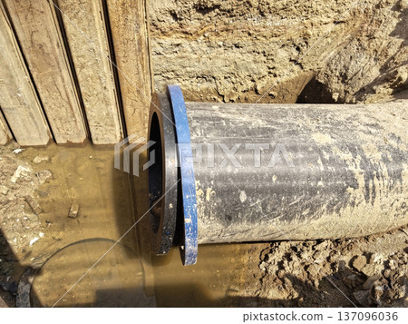 Close-up view of pipe with a blue fitting and water in a trench 137096036