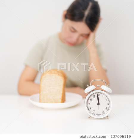 hungry woman with whole wheat bread and clock. concept of intermittent fasting, IF, meal, Time to eat, choosing healthy carbohydrates, balanced diet and weight loss management, Nutrition schedule hungry woman with whole wheat bread and clock. concept of intermittent fasting, IF, meal, Time to eat, choosing healthy carbohydrates, balanced diet and weight loss management, Nutrition schedule 137096119