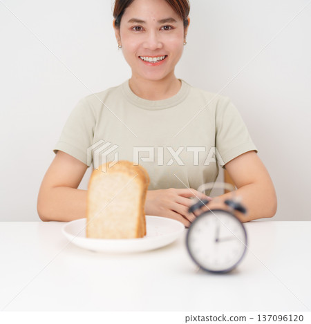 Happy smiling woman with whole wheat bread and alarm clock. concept of intermittent fasting, IF, meal timing, and choosing healthy carbohydrates for a balanced diet and weight loss management Happy smiling woman with whole wheat bread and alarm clock. concept of intermittent fasting, IF, meal timing, and choosing healthy carbohydrates for a balanced diet and weight loss management 137096120