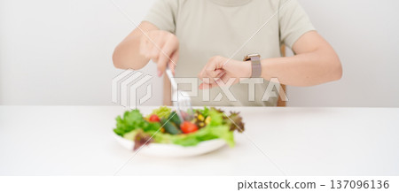 happy smiling woman with fresh organic vegetables plate and checking time. intermittent fasting, IF, nutrition control, weight loss, clean eating, Healthy food eating, Wellness, dieting and lifestyle happy smiling woman with fresh organic vegetables plate and checking time. intermittent fasting, IF, nutrition control, weight loss, clean eating, Healthy food eating, Wellness, dieting and lifestyle 137096136