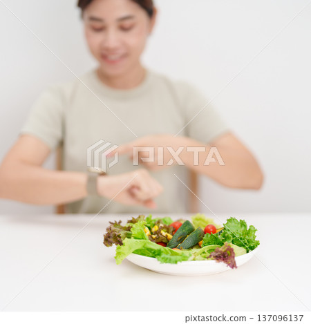happy smiling woman with fresh organic vegetables plate and checking time. intermittent fasting, IF, nutrition control, weight loss, clean eating, Healthy food eating, Wellness, dieting and lifestyle 137096137