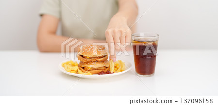 woman eating Juicy beef burger with melted cheddar cheese, potato chips and carbonated Soft drinks. Unhealthy, High calorie, Fast food craving, Obesity, diet, weight loss, junk food and lifestyle 137096158