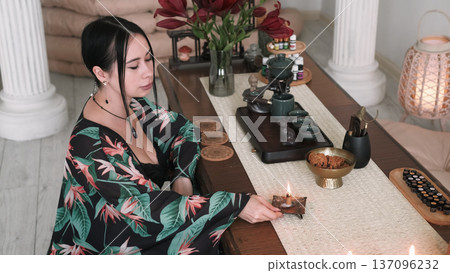Aroma meditation. Spiritual practice. Woman holding blowing burning candle placed on table mental calming ritual aesthetic atmosphere. Aroma meditation. Spiritual practice. Woman holding blowing burning candle placed on table mental calming ritual aesthetic atmosphere. 137096232