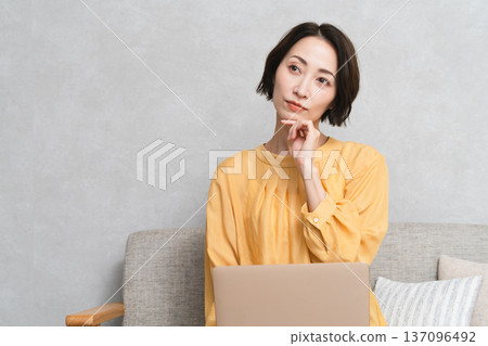 一位女士坐在沙發上使用筆記型電腦。 （生活照） 137096492