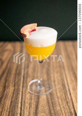 Alcoholic drink. Aperitif glass. Bright yellow tasty juice cocktail with white foam layer garnished with aromatic dried fruit slice. Alcoholic drink. Aperitif glass. Bright yellow tasty juice cocktail with white foam layer garnished with aromatic dried fruit slice. 137096608