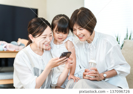 Three-generation family relaxing while looking at smartphone, family (app, video, SNS) Three-generation family relaxing while looking at smartphone, family (app, video, SNS) 137096726