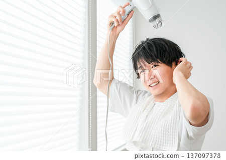 一位年輕的亞洲男子洗完澡後正在用吹風機吹乾頭髮。 137097378