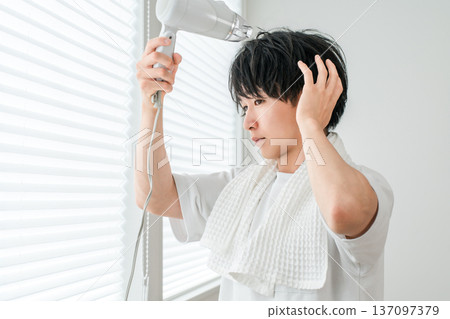 一位年輕的亞洲男子洗完澡後正在用吹風機吹乾頭髮。 137097379