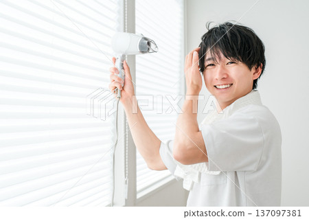 一位年輕的亞洲男子洗完澡後正在用吹風機吹乾頭髮。 137097381