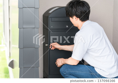 一名男子在他家門口打開一個快遞箱。 一名男子在他家門口打開一個快遞箱。 137098166