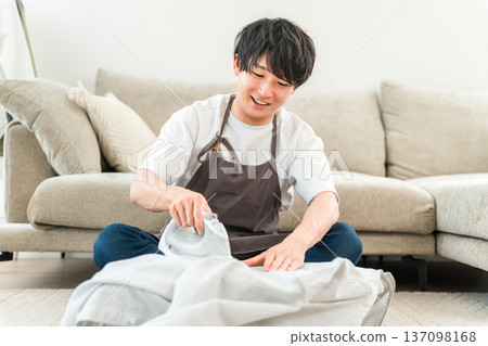 一個男人穿著圍裙在客廳熨襯衫 137098168