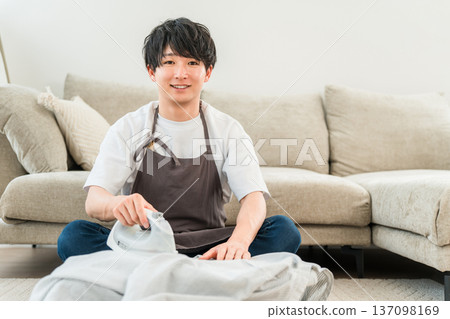 一個男人穿著圍裙在客廳熨襯衫 137098169