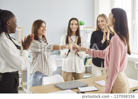 Two young businesswomen shaking hands while team members applauding 137098336