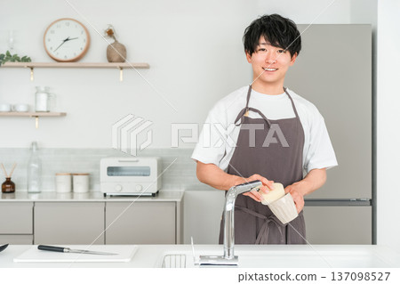 Young Asian man in an apron washing dishes in the kitchen 137098527
