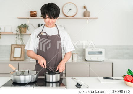 Young Asian man in an apron cooking in the kitchen Young Asian man in an apron cooking in the kitchen 137098530