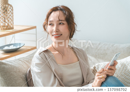 Asian woman sitting on the sofa in the living room and looking at her smartphone 137098702