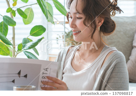 一位穿著時尚的亞洲女性在家中客廳閱讀雜誌。 一位穿著時尚的亞洲女性在家中客廳閱讀雜誌。 137098817