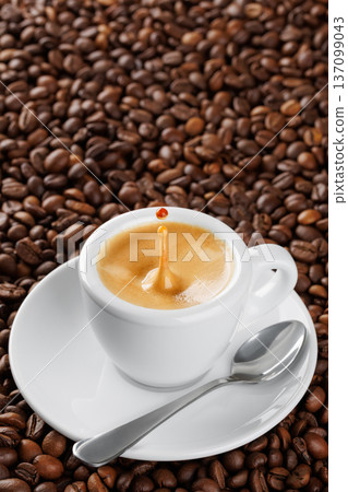 Small white espresso cup with splash and drop, brimming with aromatic coffee resting on bed of roasted beans 137099043