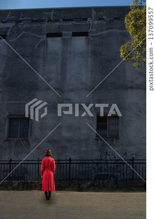 A woman standing in front of a dilapidated building 137099557