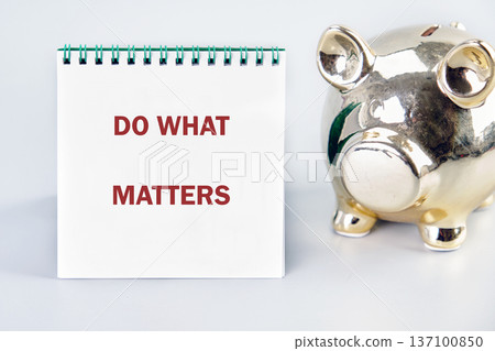 Golden piggy bank by DO WHAT MATTERS notebook on white. Inspires mindful saving and purposeful living Golden piggy bank by DO WHAT MATTERS notebook on white. Inspires mindful saving and purposeful living 137100850