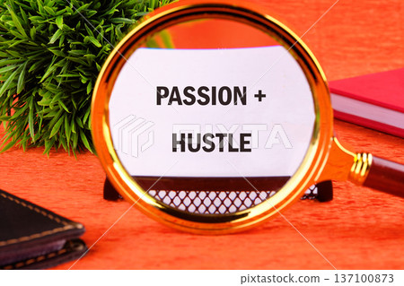 A magnifying glass centers on a white paper declaring Passion and Hustle, set on an orange desk with a green plant and red book nearby. This captures motivation A magnifying glass centers on a white paper declaring Passion and Hustle, set on an orange desk with a green plant and red book nearby. This captures motivation 137100873