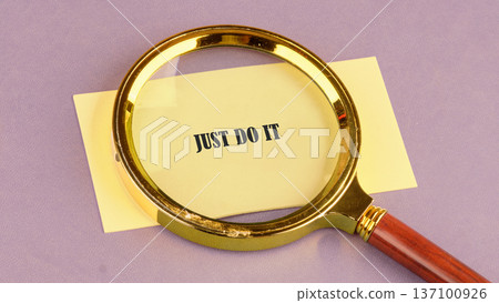 Just Do It on yellow paper, enlarged by a gold magnifier resting on a lavender surface Just Do It on yellow paper, enlarged by a gold magnifier resting on a lavender surface 137100926