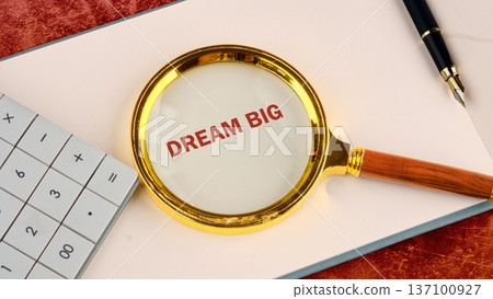 A golden magnifying glass spotlights the words DREAM BIG on crisp white paper 137100927