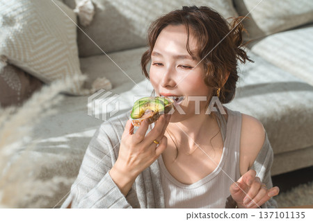 Stylish young Asian woman eating at the living room table 137101135