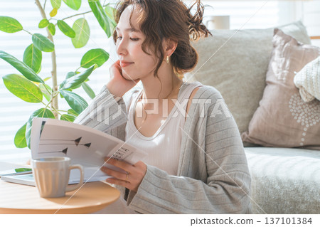 A stylish Asian woman reading a magazine in the living room 137101384